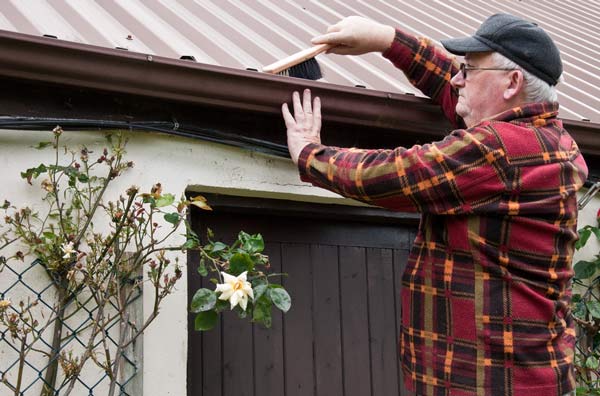 A picture of a man cleaning his eavestroughs.